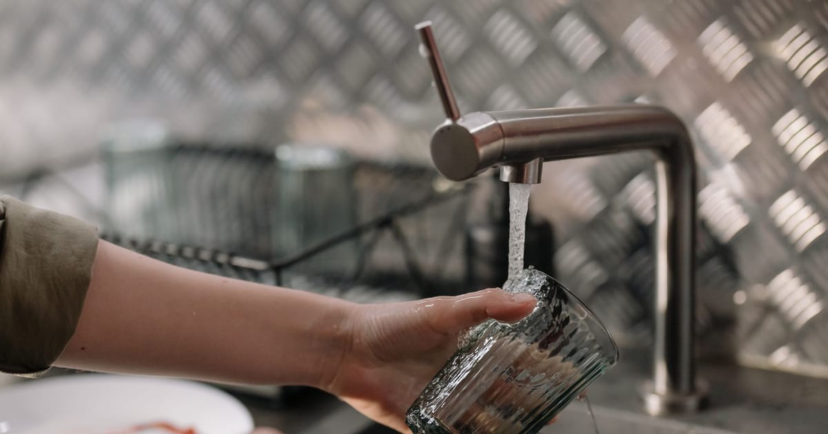 A kitchen tap filling a glass beside a small handheld TDS meter.